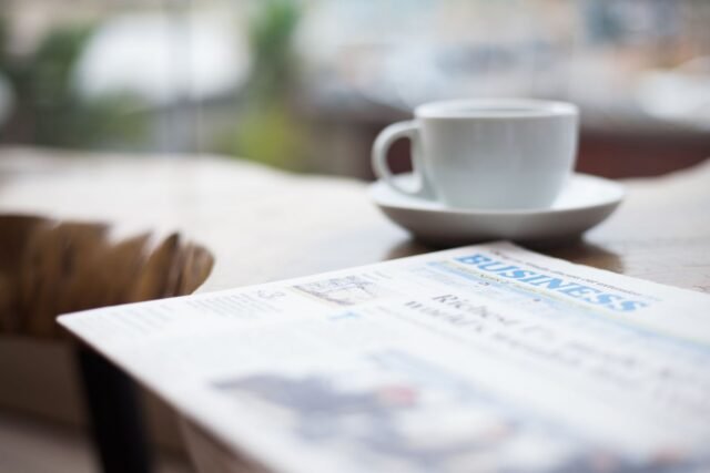 Ziar împăturit și o ceașcă de cafea pe o masă de lemn, într-o dimineață liniștită