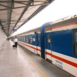 Călător cu o valiză pe peronul unei gări europene, așteptând sosirea trenului