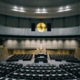 Sală de plen goală a unui parlament, cu băncile aranjate în semicerc și pupitrul central