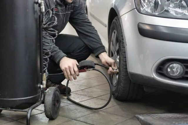 Șofer care verifică presiunea în anvelopa unei mașini, într-o dimineață rece